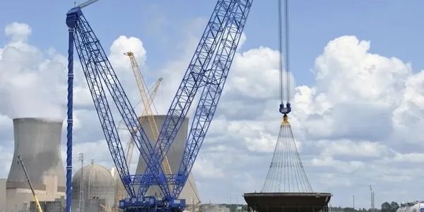 Large cranes lifting construction materials near a power plant.