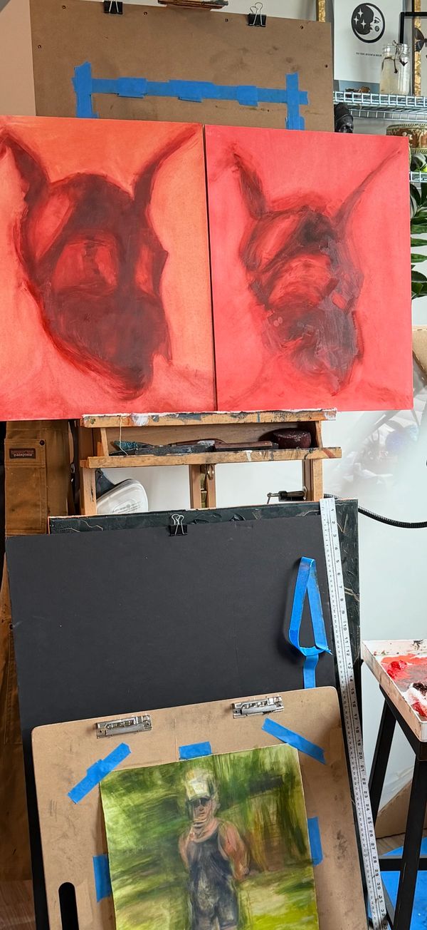 Two red abstract paintings of dog faces on an easel with a blurred portrait below.