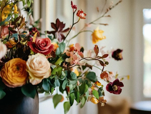 A vibrant bouquet of mixed flowers in a dark vase with a blurred background.