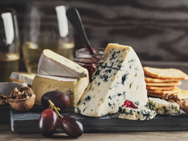 A cheese platter with blue cheese, grapes, walnuts, crackers, and jam.