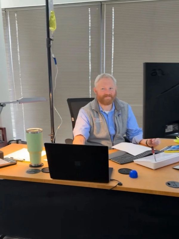 Man with red beard sitting at desk with computer and papers.
