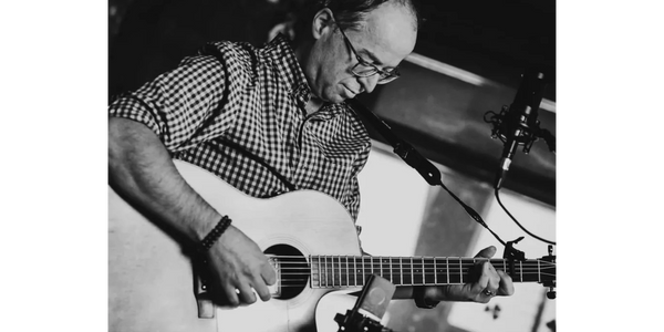 Man playing acoustic guitar and singing into microphones.
