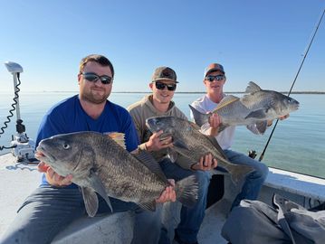 Three men proudly display large fish caught on a calm lake.