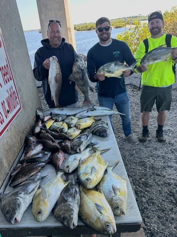 Three men proudly displaying their diverse catch of fish by the water.