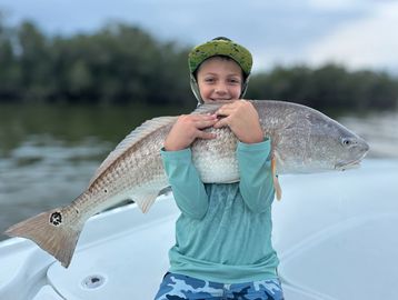 A young boy proudly holds a large fish on a boat.