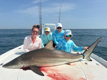 Family posing with a large caught shark on a boat in the ocean.