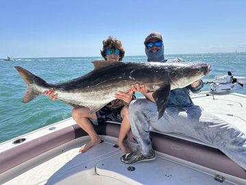 Two men on a boat proudly holding a large fish they caught.