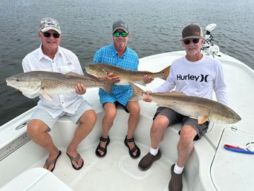 Three men on a boat proudly holding large fish they caught.