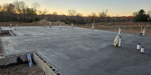Newly poured concrete foundation slab with plumbing pipes.