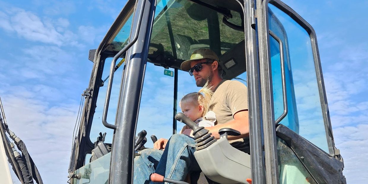 A man and child inside a construction vehicle on a bright day.