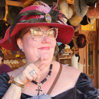 Woman in a red feathered hat and leopard print glasses smiling.