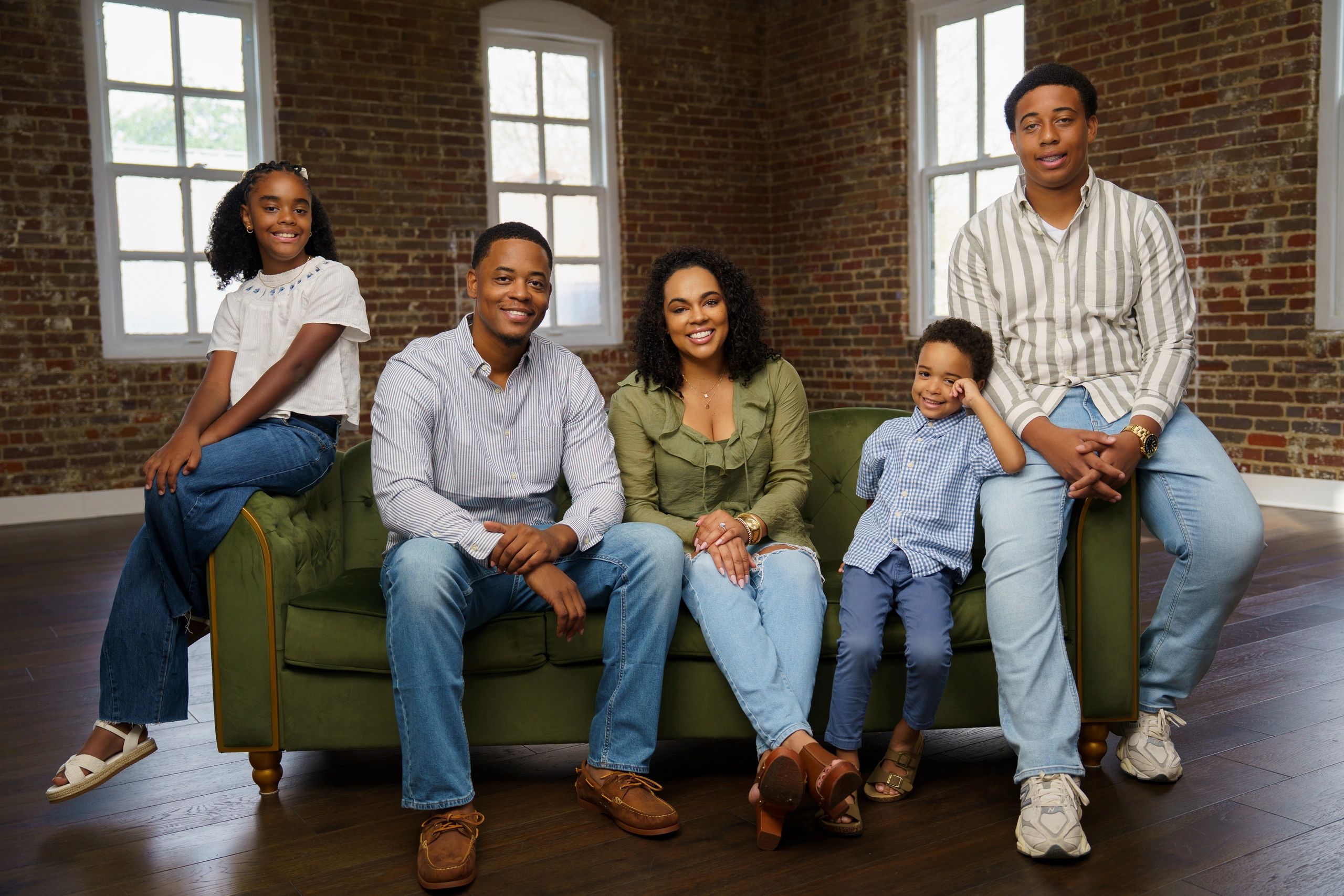 Happy family sitting on a green couch in a brick-walled room.