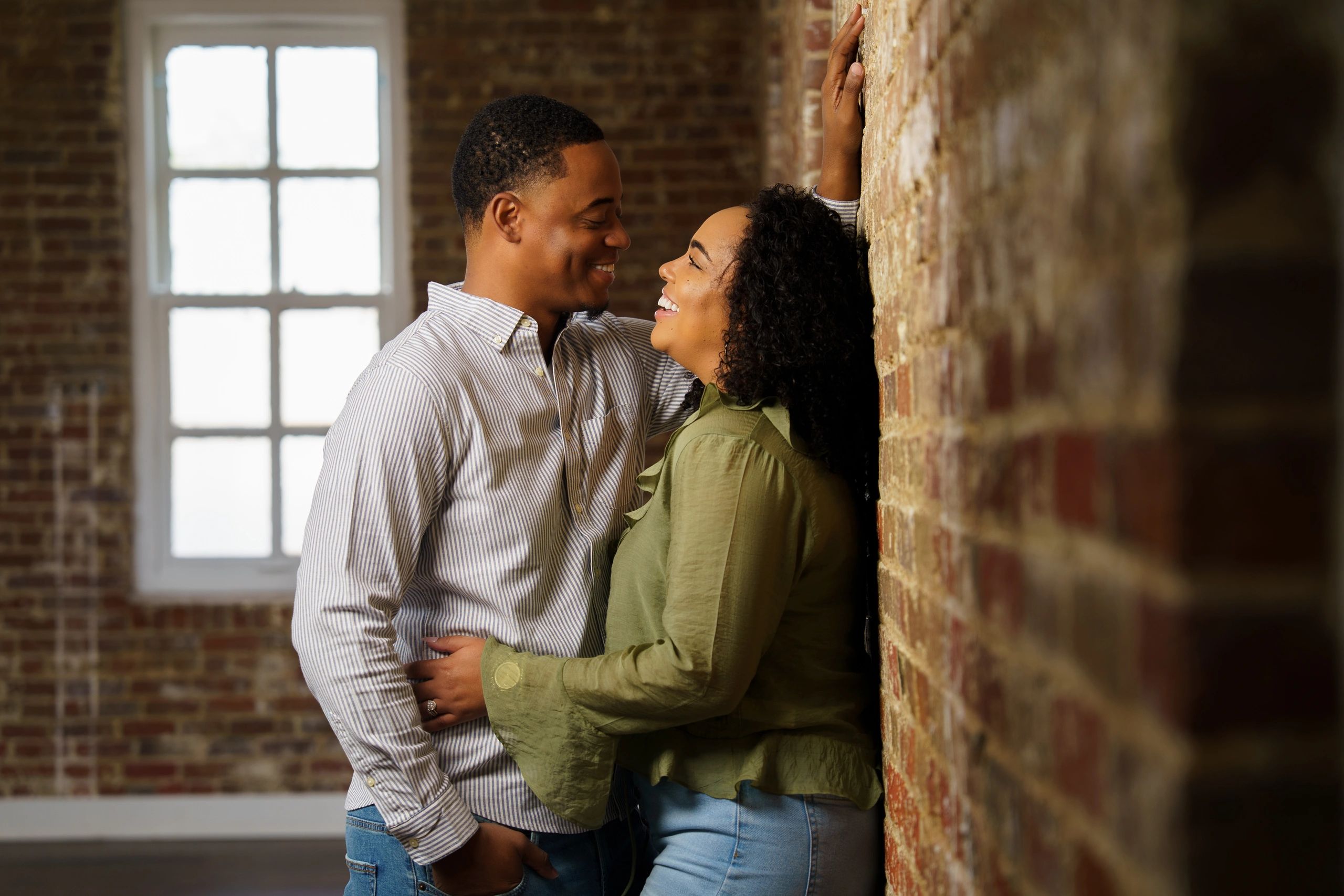 Couple sharing a joyful, affectionate moment by a brick wall.