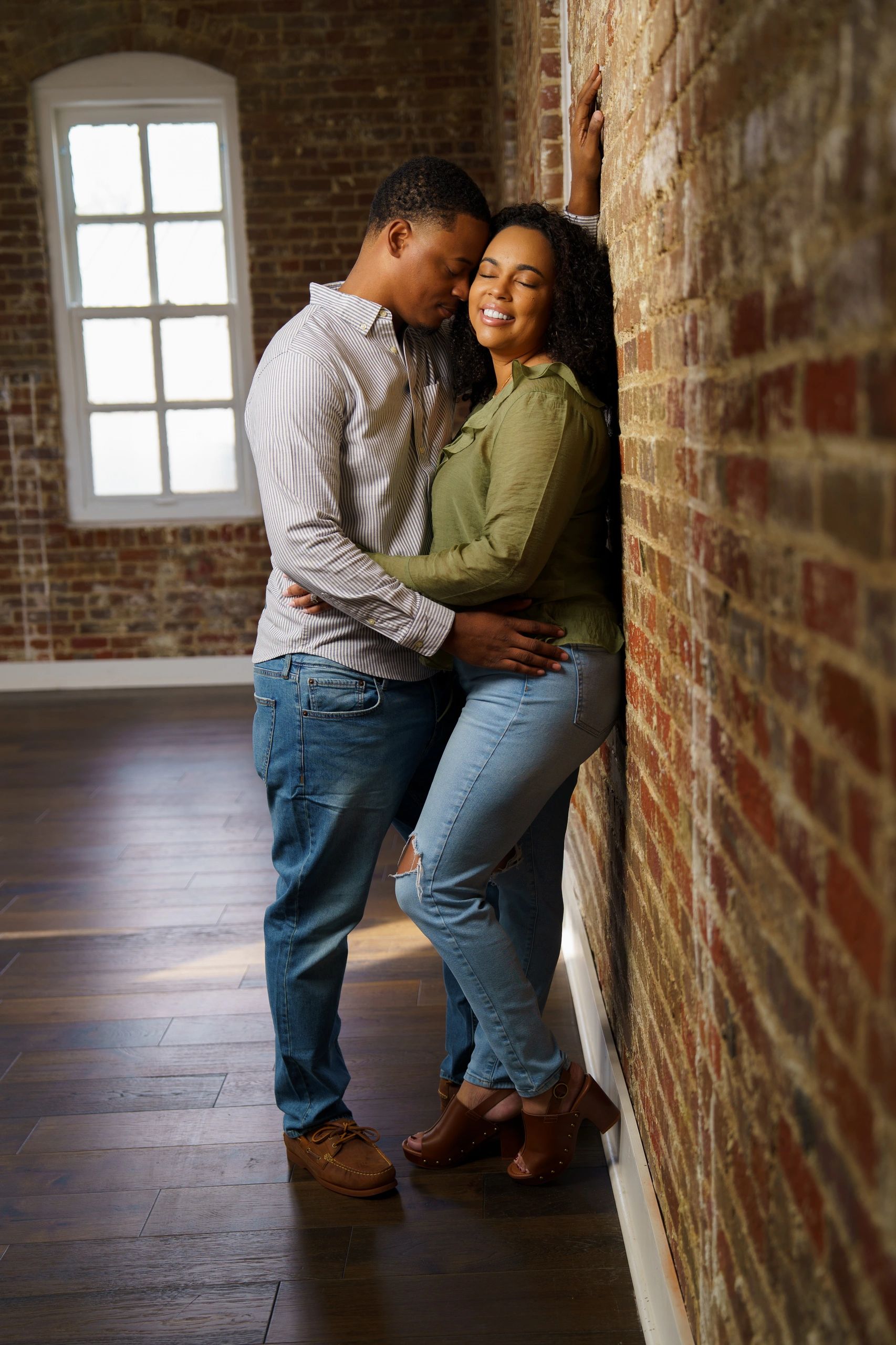 Couple embracing against a brick wall.