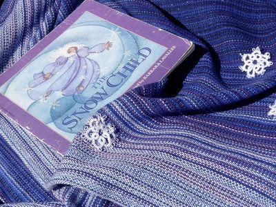 A blue and white pinstriped piece of fabric with the book "The Snow Child" and tatted snowflakes.