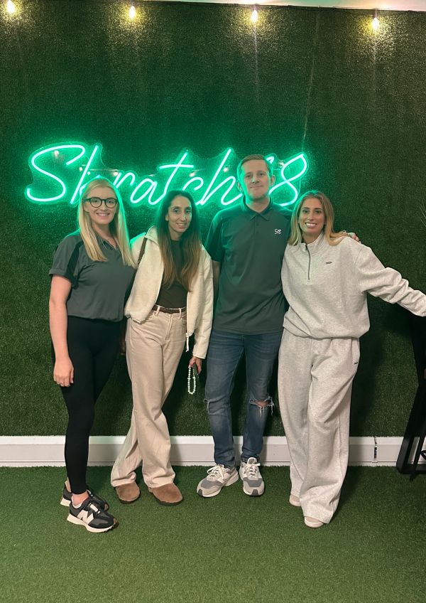 Four friends posing in front of a green wall with neon sign.