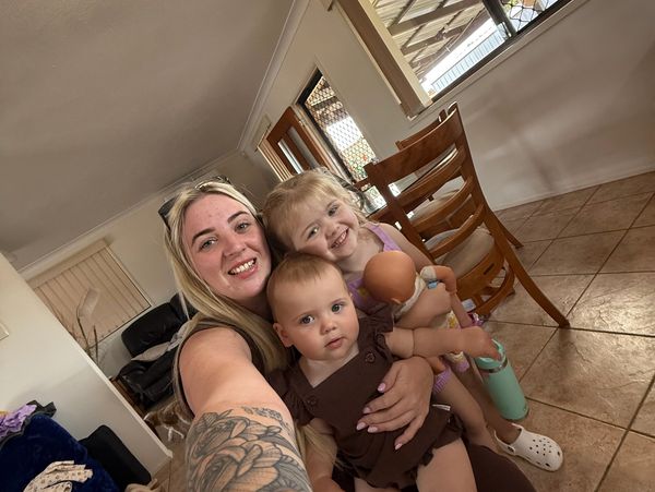 A woman with two children smiling indoors for a selfie.