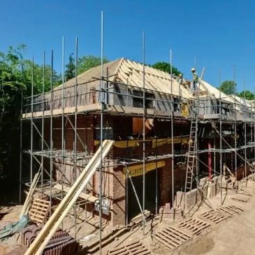 House under construction with scaffolding and workers on roof.