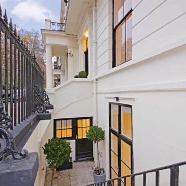 Elegant white house exterior with basement entrance and plants.