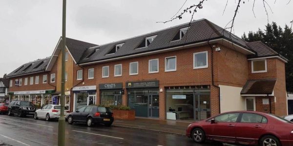 Street view of a commercial building with parked cars on a rainy day.