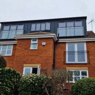 Red brick house with modern upper floor addition and bushes.