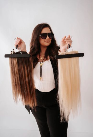 Woman holding two hair extensions, one dark and one blonde.
