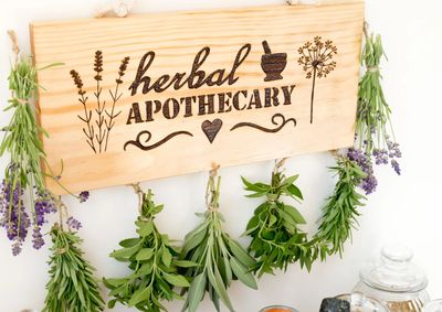 Wooden herbal apothecary sign with hanging fresh herbs.