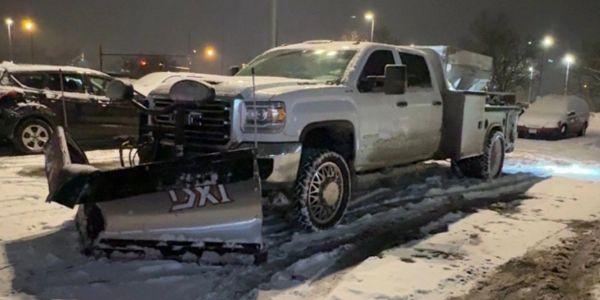 White truck with snowplow parked in snow at night.