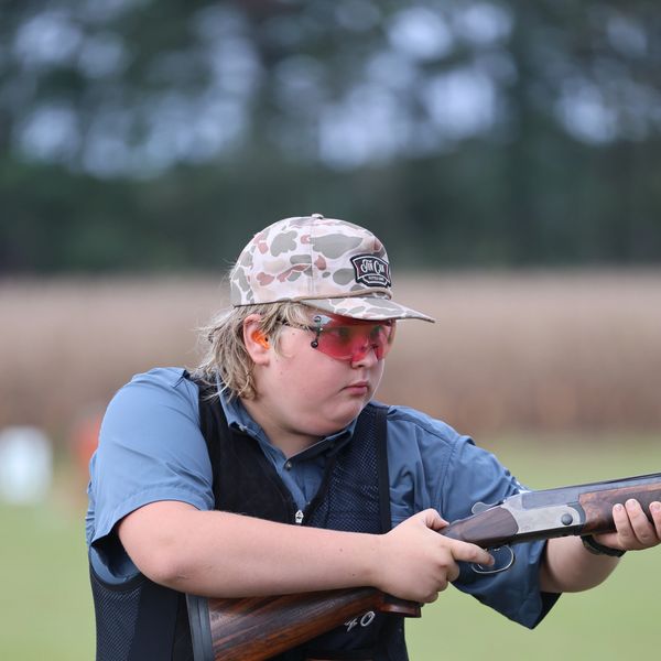 Young person in camouflage hat aiming shotgun during shooting practice.