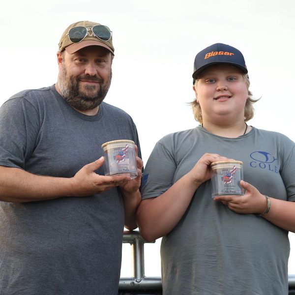 Two people holding clear containers with lids, smiling at the camera outdoors.