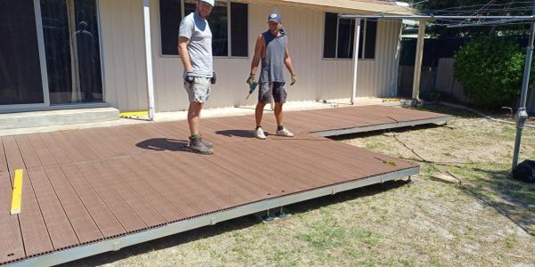 Two men working on installing a wooden deck outside a house.