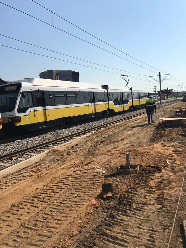 A yellow and white train on tracks next to a construction site with a worker.