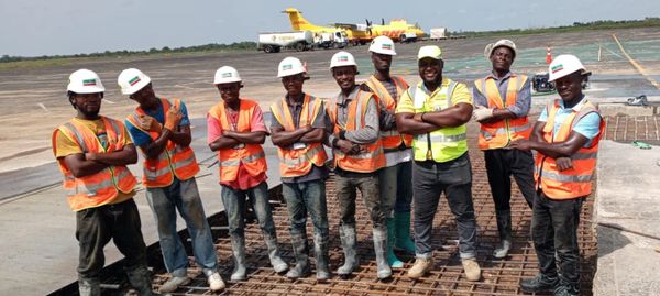 Group of construction workers in safety gear standing on a construction site with an airplane in the background.