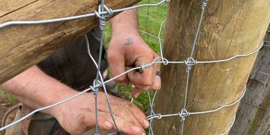 Professional fence installer tying a termination knot around a fence post in Central Oregon