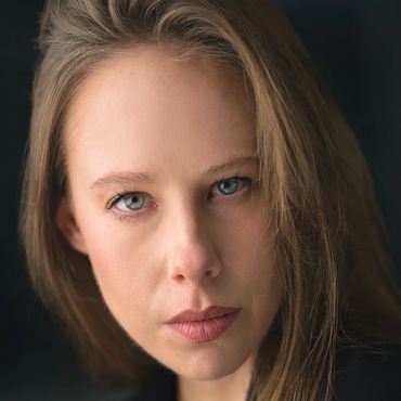 Close-up of a serious woman with blue eyes and light brown hair.