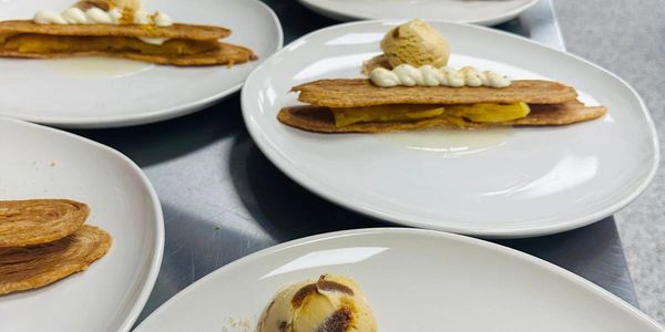 Rows of plated desserts with pastry, cream, and ice cream in a professional kitchen.