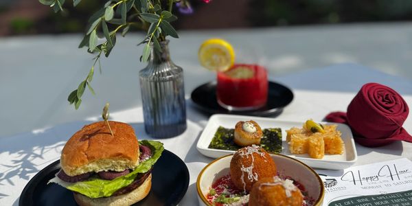 A meal with a burger, appetizers, a drink, and a flower vase on a white tablecloth.