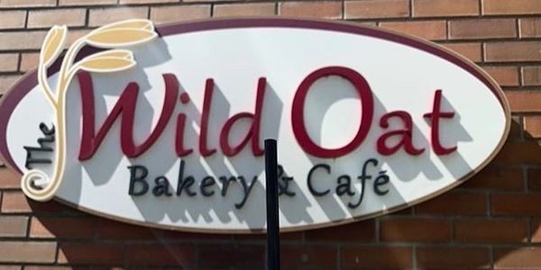 Latte in front of The Wild Oat Bakery & Cafe sign
