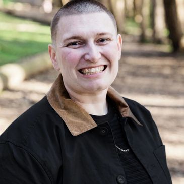 Person with short hair smiling outdoors in a casual jacket.