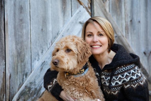 Woman smiling with a fluffy dog in front of a rustic wooden door.