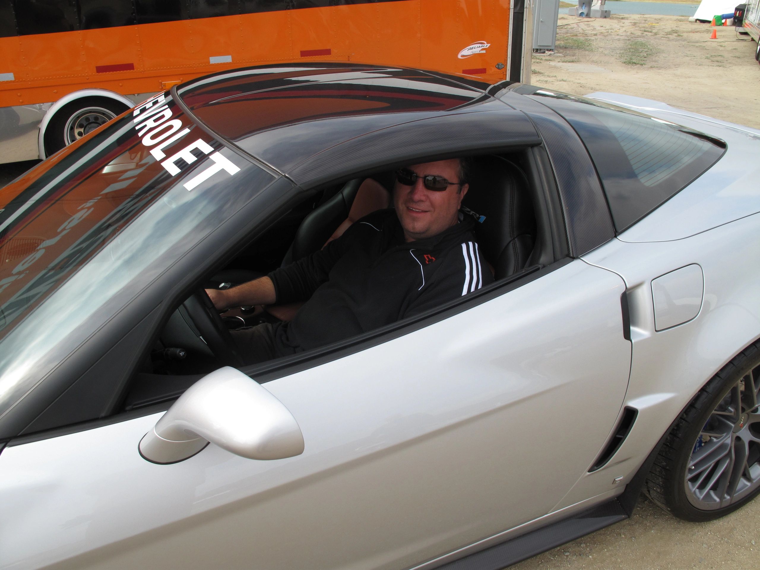 A man in sunglasses sits inside a white Chevrolet sports car.