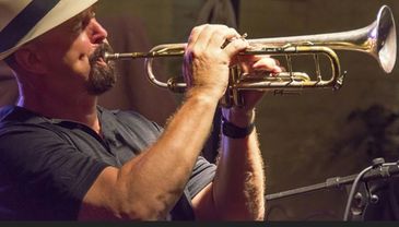 Man playing trumpet passionately in a dimly lit setting.