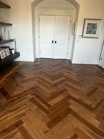 Room with dark herringbone wood flooring and white double doors.