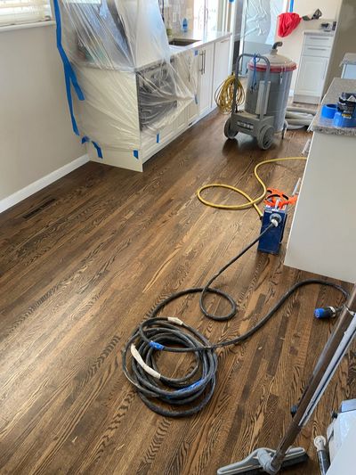 Newly refinished hardwood floor in a kitchen with tools and plastic-covered cabinets.