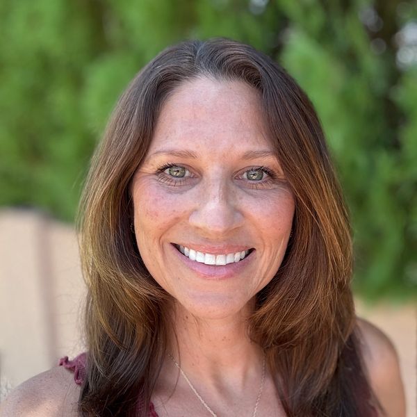 Smiling woman with brown hair outdoors.
