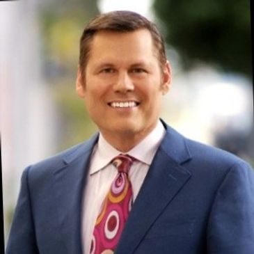 Man in a blue suit and colorful tie smiling outdoors.