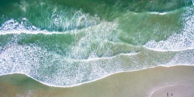 Aerial view of waves gently crashing onto a sandy beach.