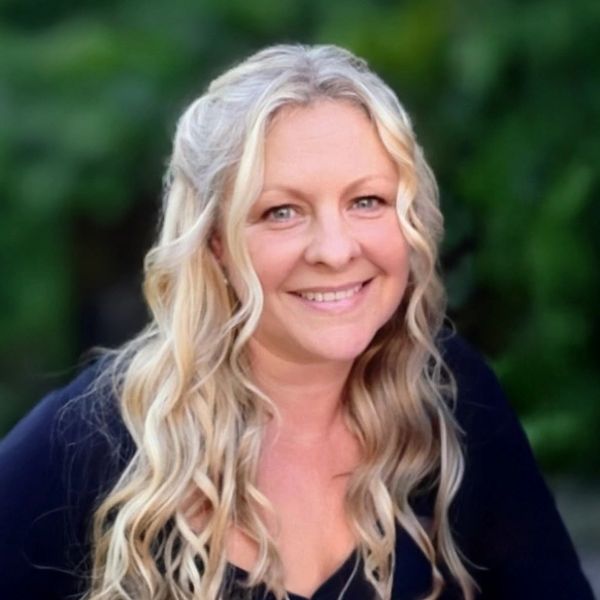 Smiling woman with long blonde wavy hair and a black top outdoors.
