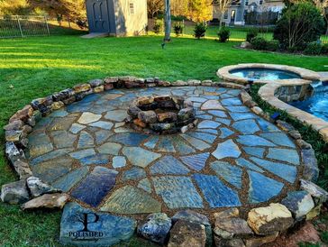 Flagstone patio with garden boulder retaining wall and firepit beside of a pool in a backyard.