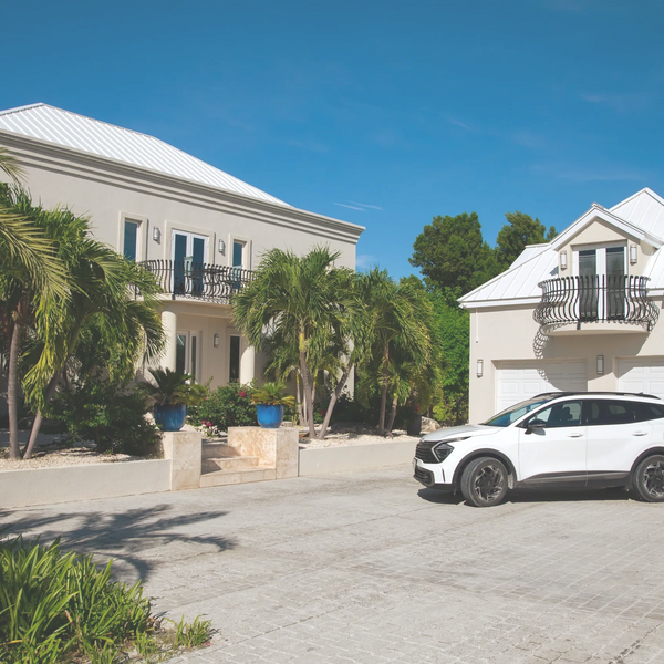 An suv parked diagonally in front of a garage in a large driveway that is in front of a large villa